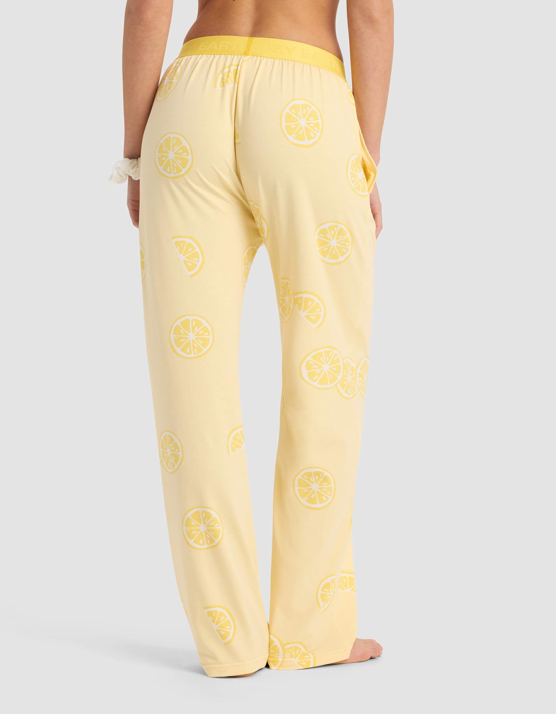 Woman wearing Cozy Earth Women's First Layer Pajama Pant in light yellow with a lemon slice pattern, elastic waistband, and relaxed fit, standing barefoot and viewed from the back.