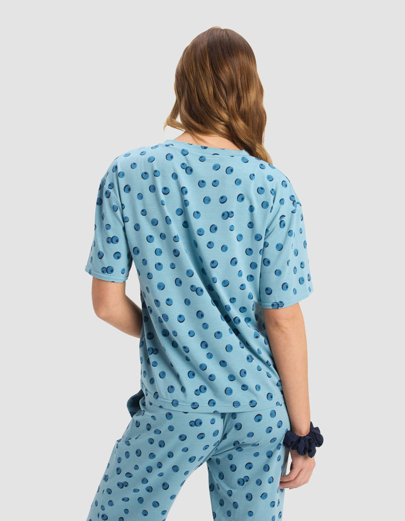 A person with wavy, light brown hair is shown from the back wearing Cozy Earth’s Women's First Layer Pajama Short Sleeve Tee in light blue with a dark blue polka dot pattern and a matching scrunchie on their left wrist.