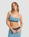 A woman with long, wavy hair wears the Cozy Earth Women's First Layer Pajama Soft Bra and matching shorts in light blue with dark blue polka dots, standing against a plain light gray background.|Color:Blueberries