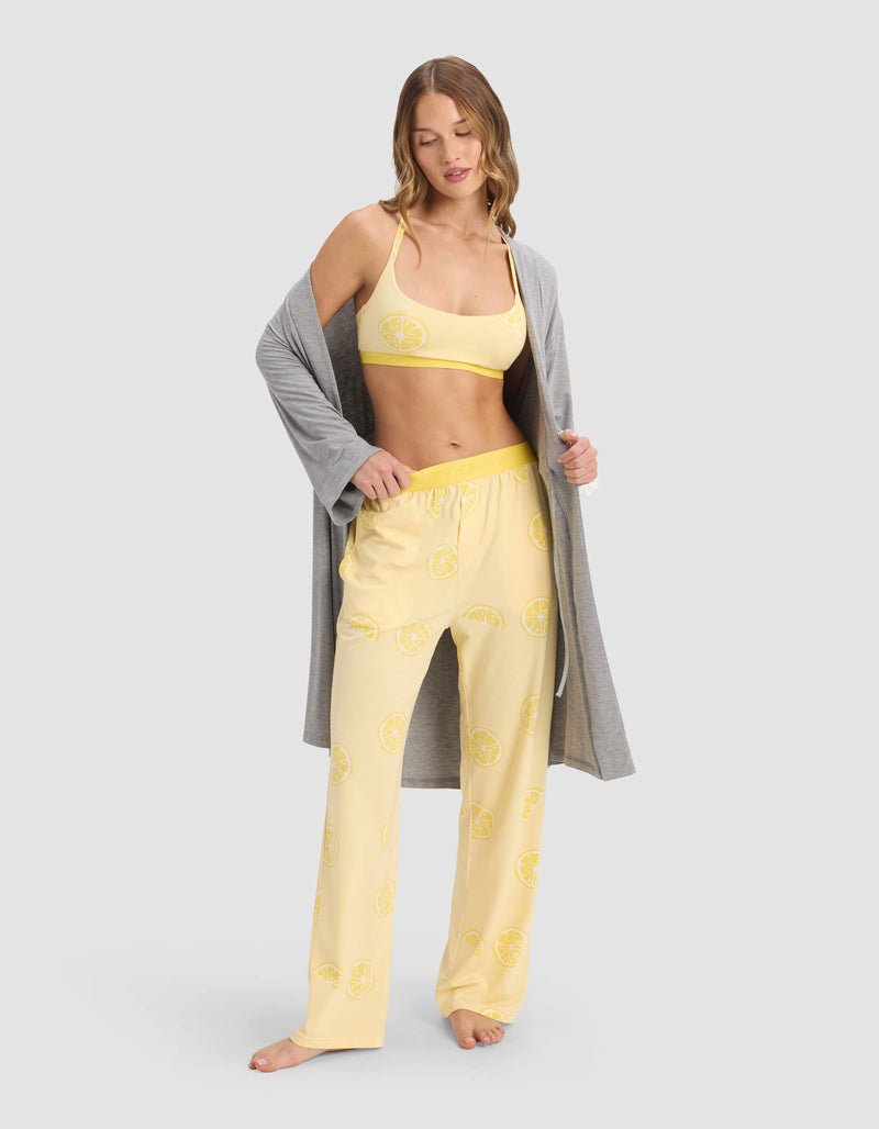 A woman poses against a light gray background wearing Cozy Earth's Women's First Layer Pajama Soft Bra under a grey robe and yellow pajama set with lemon slice prints.