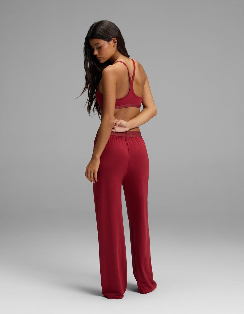 A person wears a maroon Cozy Earth Women’s First Layer Pajama Soft Bra & Pajama Pant Set, featuring a racerback bralette and wide-leg pants.