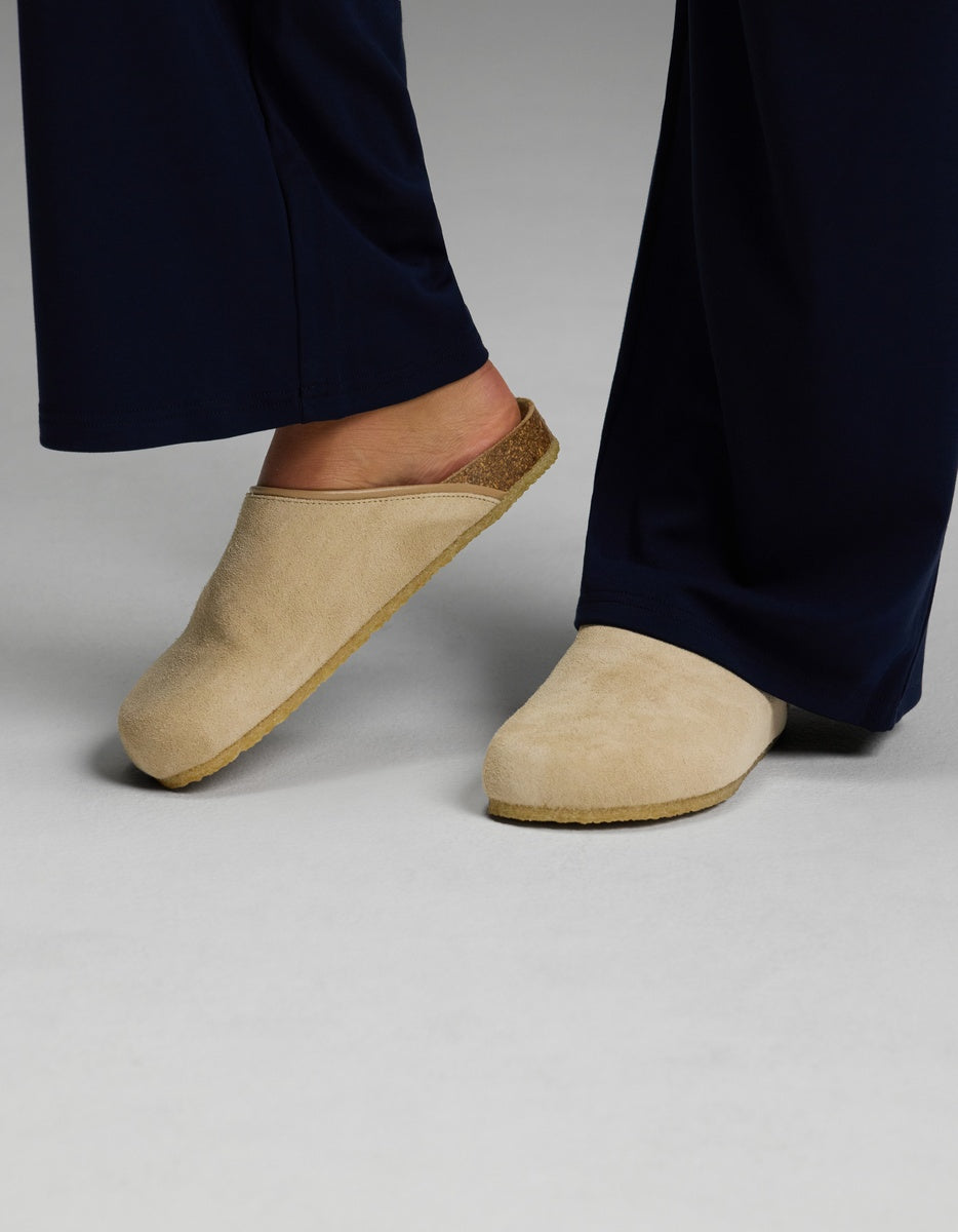 A person wearing navy blue pants and Cozy Earth’s Lakehouse Clog in Suede stands on a light gray surface.|Color:Sandalwood