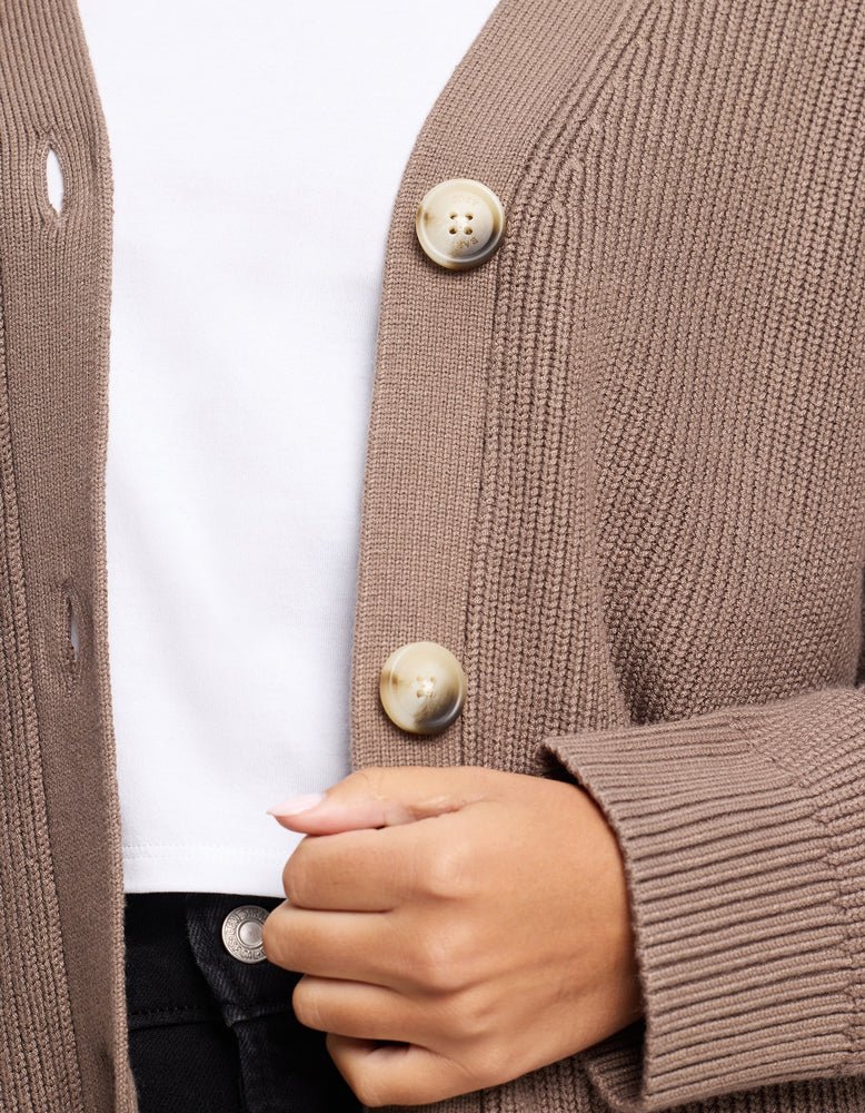 A close-up of a person in the Cozy Earth Oversized Classic Cardigan, featuring large buttons, worn over a white shirt and black pants, with their hand holding the cardigan near the buttons.