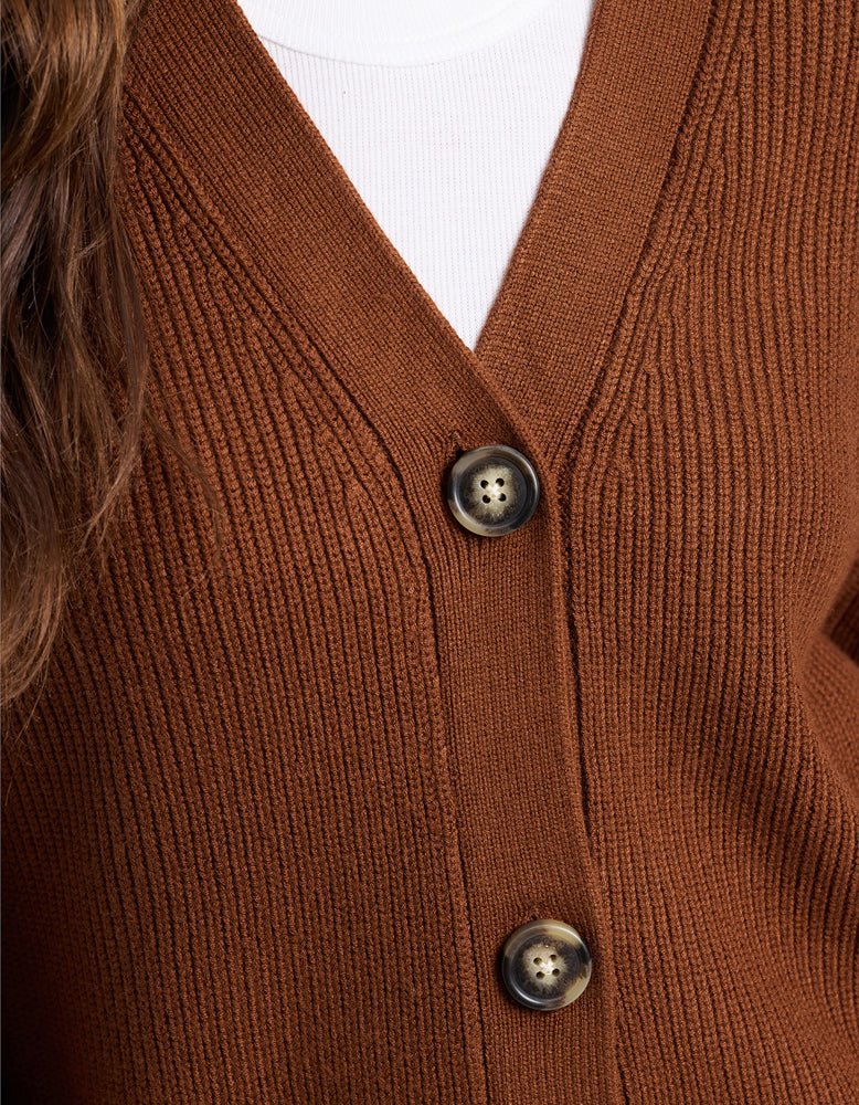 Close-up of a person wearing Cozy Earth's Oversized Classic Cardigan in ribbed brown with two dark buttons over a white top. Part of long brown hair is visible on the left side.