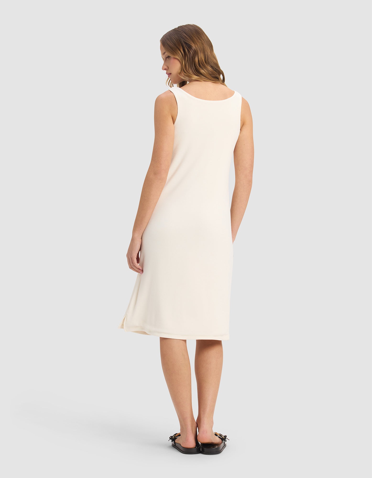 A woman faces away, wearing the Cozy Earth Women’s Bamboo Rib-Knit V-Neck Tank Lounge Dress in cream and black embellished flats, set against a plain light gray background.