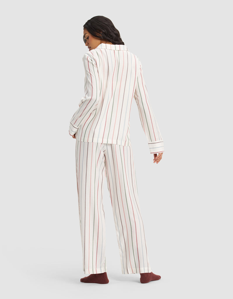 A person faces away, wearing the Cozy Earth Women's Soft Woven Long Sleeve Pajama Set in white with red and gray vertical stripes and dark red socks, set against a plain light gray background.