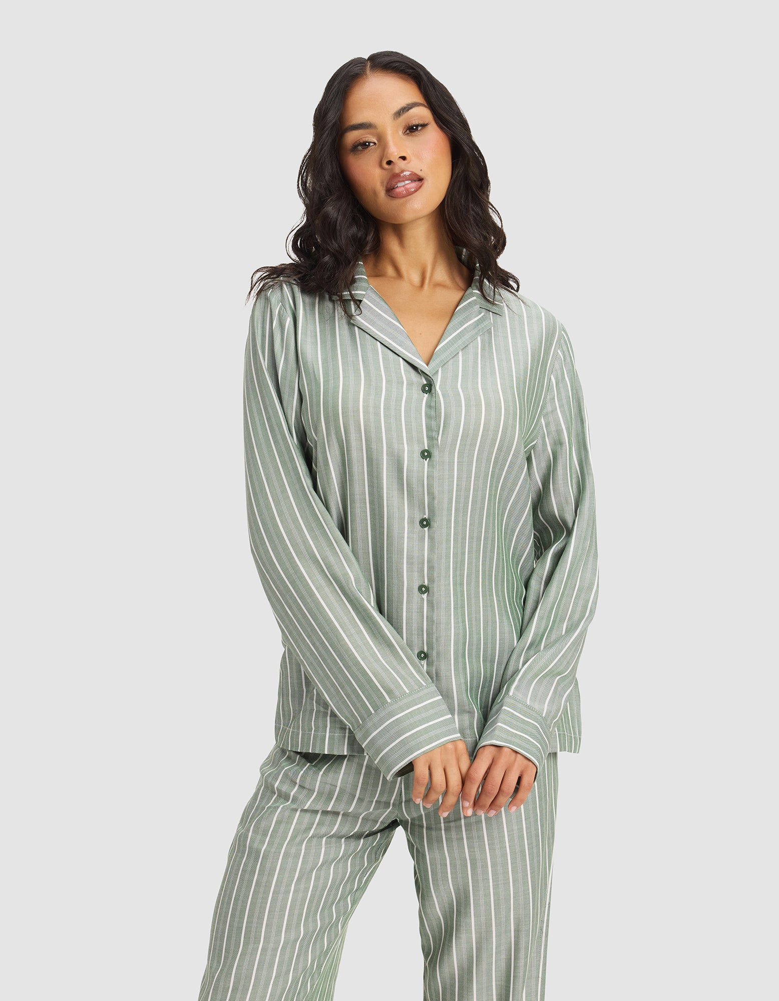 A woman with long dark hair wears the Cozy Earth Women's Soft Woven Long Sleeve Pajama Set in light green with white vertical stripes, standing against a plain light background.