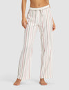 A woman models Cozy Earth’s Women's Soft Woven Pajama Pant—loose-fitting, white with vertical pink and gray stripes—barefoot against a simple backdrop.|Color:Cottage Stripe