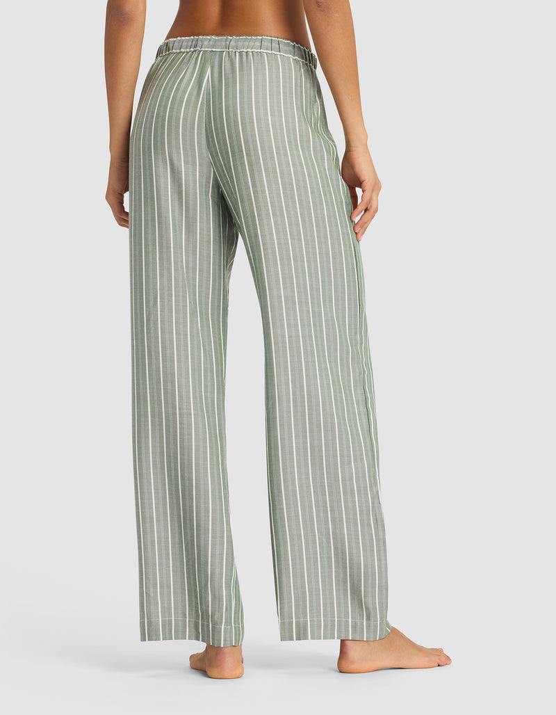 A person stands barefoot, facing away, wearing Cozy Earth's Women's Soft Woven Pajama Pant in loose green and white vertical stripes with an elastic waistband against a plain light background.