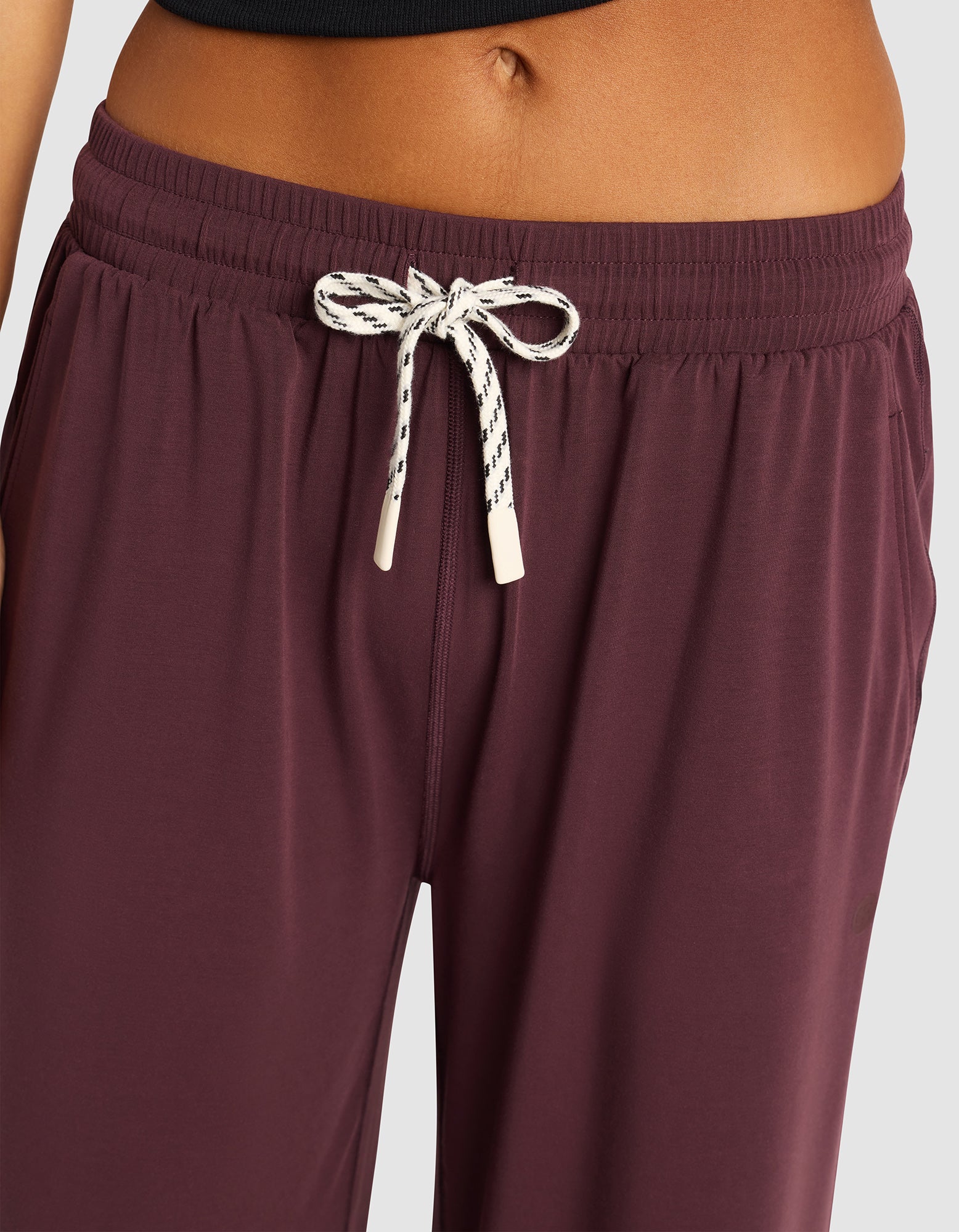 Close-up of a person wearing Cozy Earth Women's Studio Cropped Wide Leg Pant in maroon with a white and black tie at the waist, paired with a black top; the midriff and both arms are partially visible.