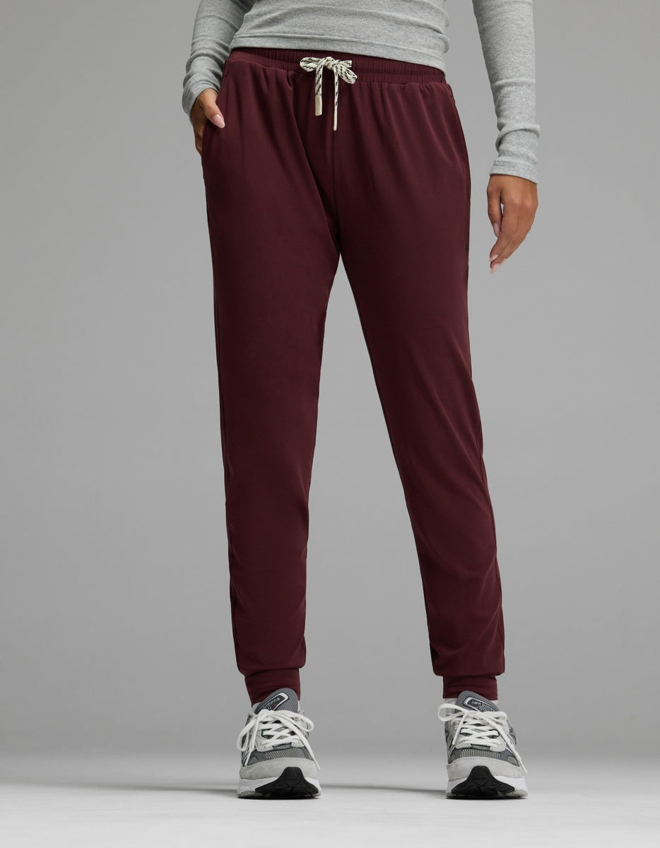 A person wearing Cozy Earth’s Women’s Studio Jogger stands against a plain gray background with hands in pockets.|Color:Burgundy