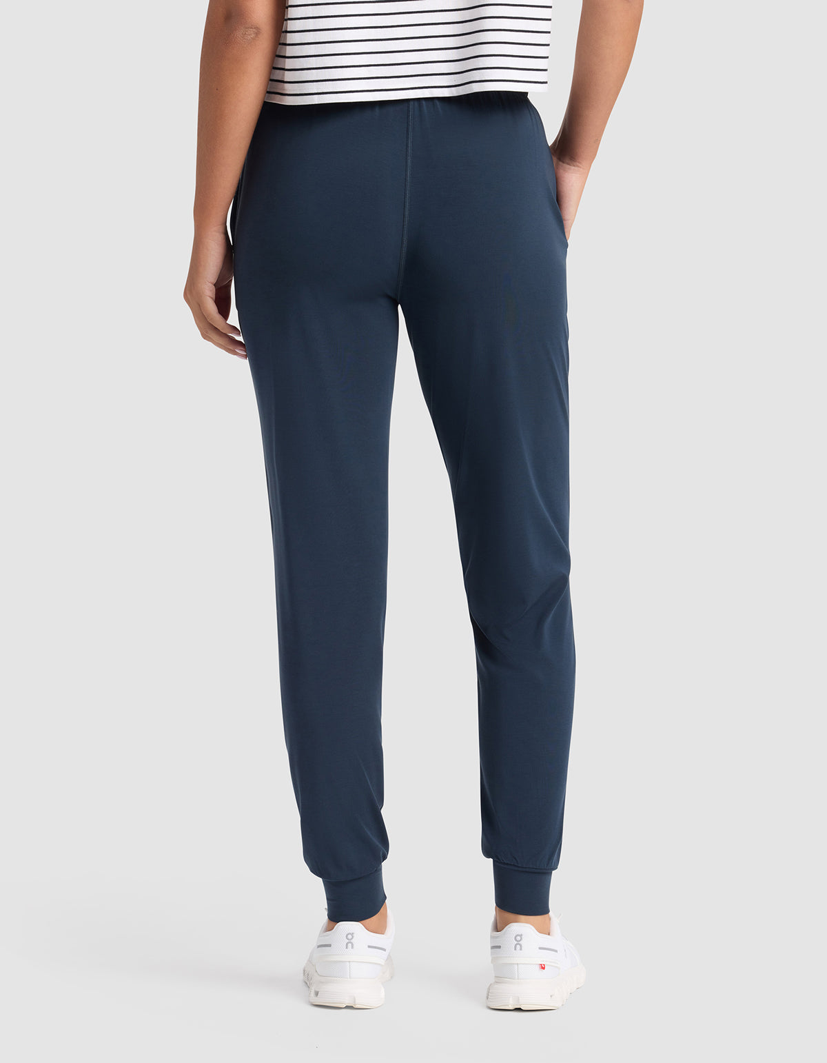 A person is shown from the back wearing Cozy Earth Women's Studio Jogger pants in navy, paired with a white and black striped shirt and white sneakers, against a plain light gray background.|Color:Eclipse