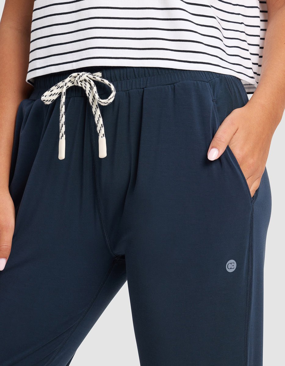 A woman wears Cozy Earth’s Women's Studio Jogger in navy blue, featuring a small pocket logo, and pairs them with a white and black striped shirt, one hand tucked into the jogger's pocket.