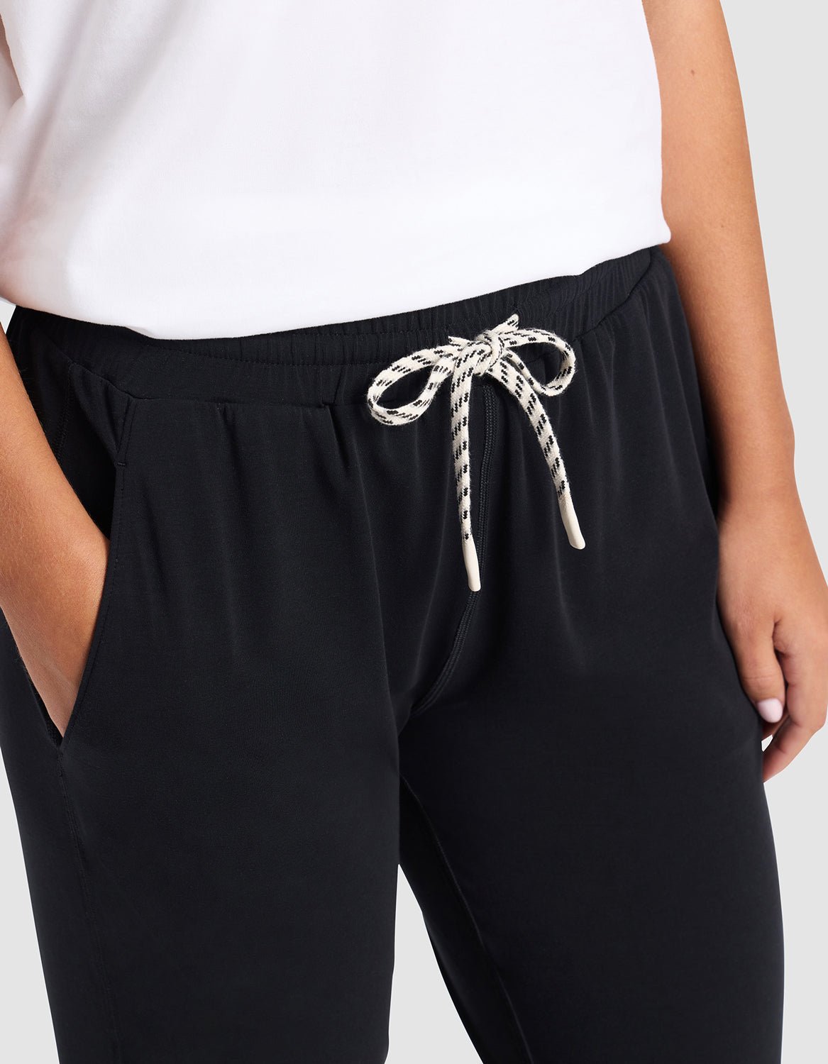 A person wearing Cozy Earth's Women's Studio Jogger in black with hands in pockets and a white top. The image is cropped to feature only the lower torso and upper legs.