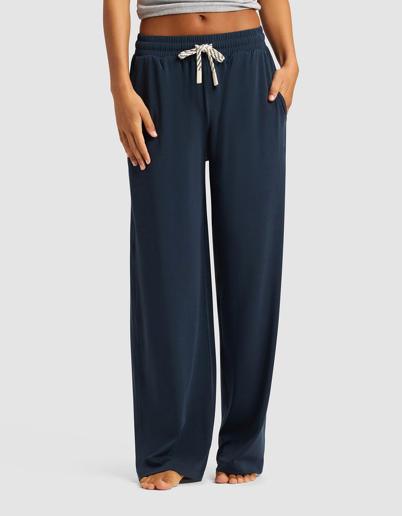 A person models the Cozy Earth Women's Studio Wide Leg Pant in navy, featuring white drawstrings. Only the lower torso and legs are visible, and they're standing barefoot against a plain light background.