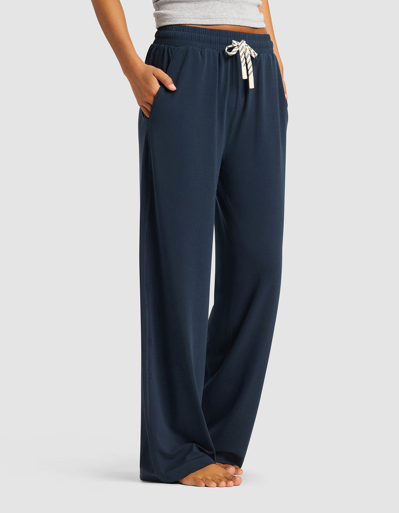 A woman wears Cozy Earth’s Women's Studio Wide Leg Pant in navy, featuring a white drawstring and pockets, standing barefoot with hands in pockets, shown from waist to feet.