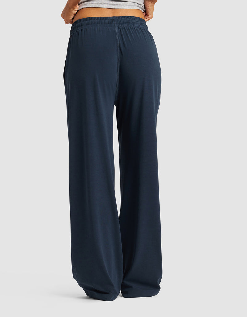 A person is seen from the back wearing Cozy Earth's Women's Studio Wide Leg Pant in dark navy blue, featuring a relaxed fit and elastic waistband, standing against a plain light background.