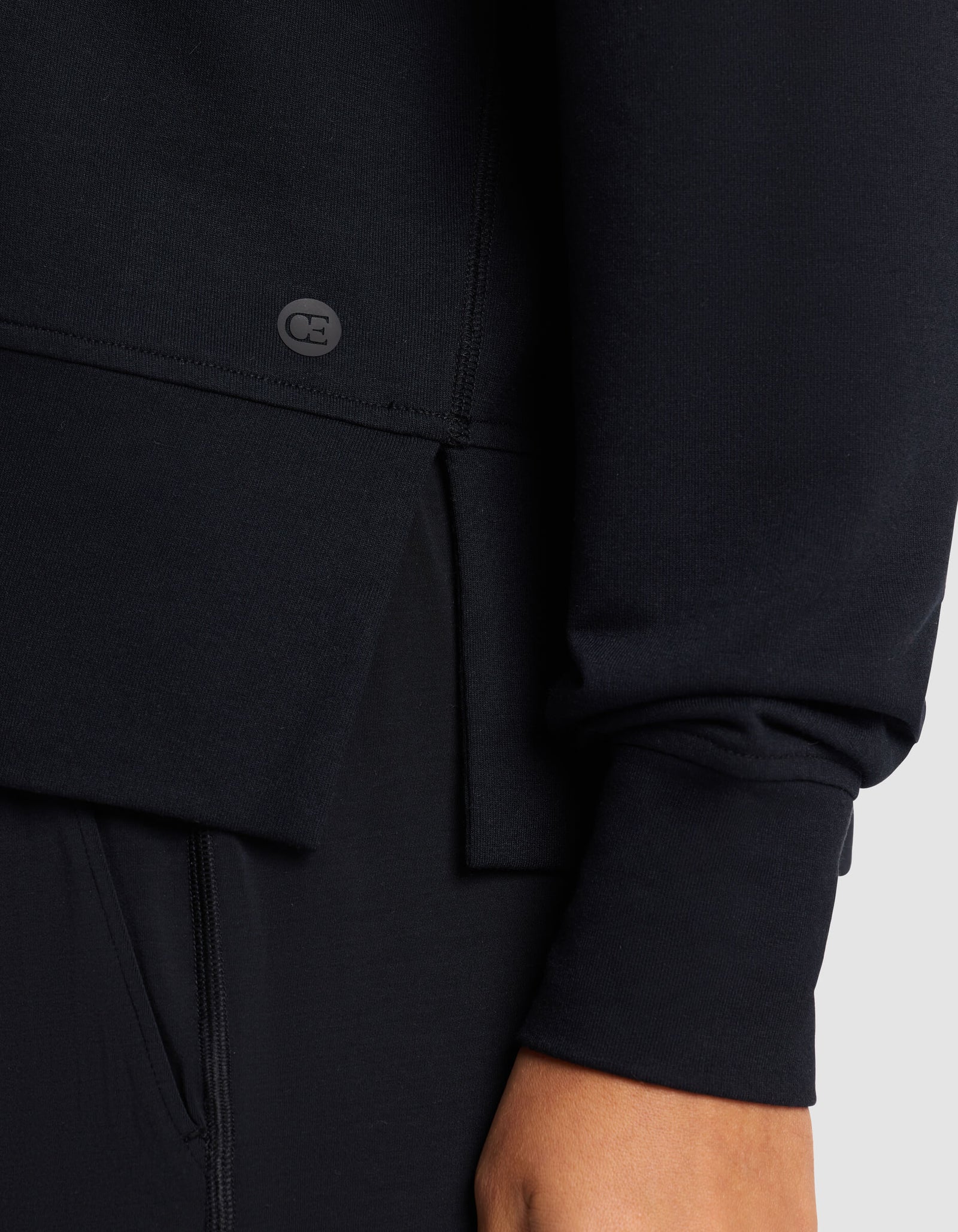 Close-up of a person wearing the Cozy Earth Women's StudioLite Crewneck in black, showing the lower sleeve, hem with a small logo, and their hand by their side.