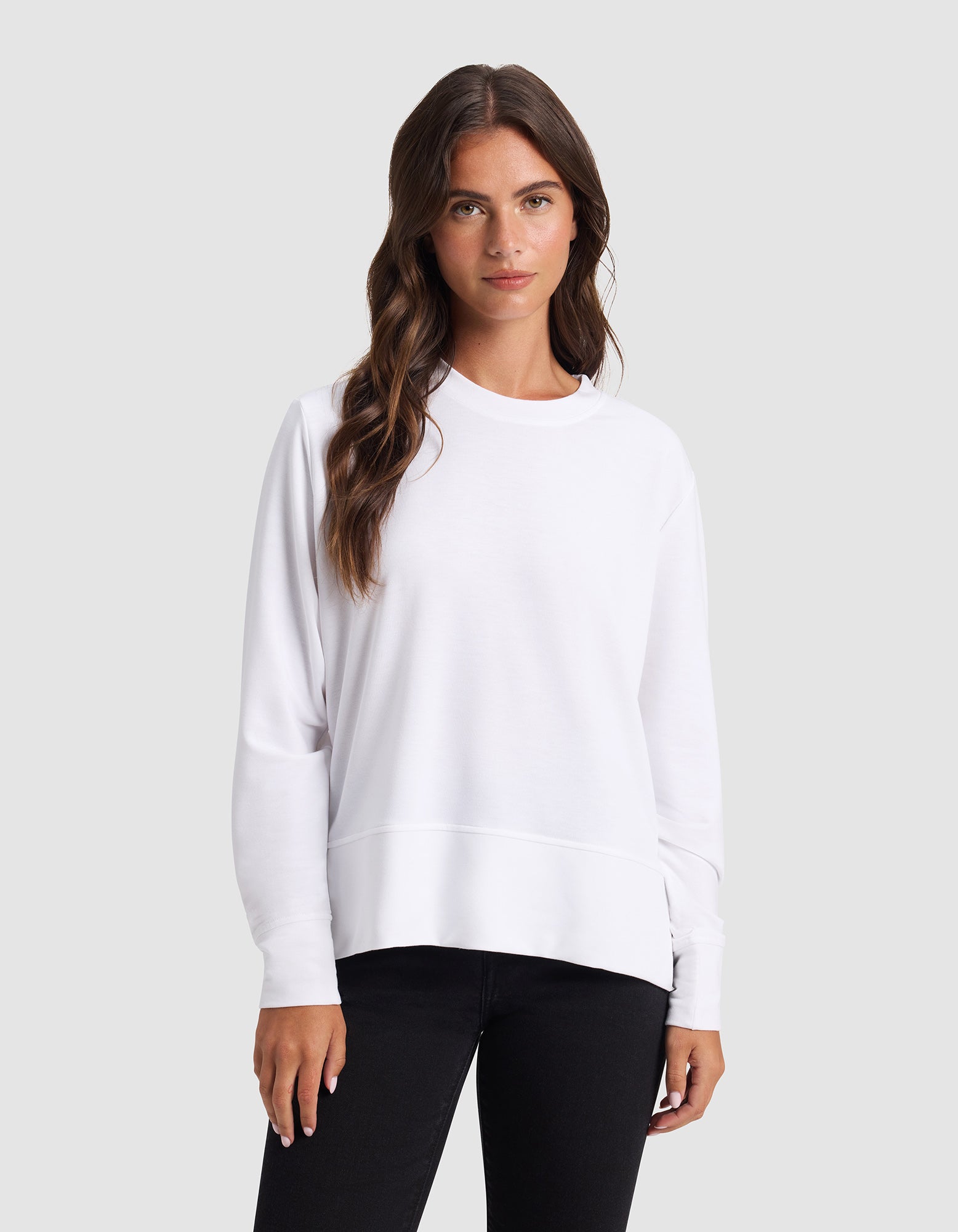 A woman with long brown hair models the Cozy Earth Women's StudioLite Crewneck, standing against a plain light gray background.