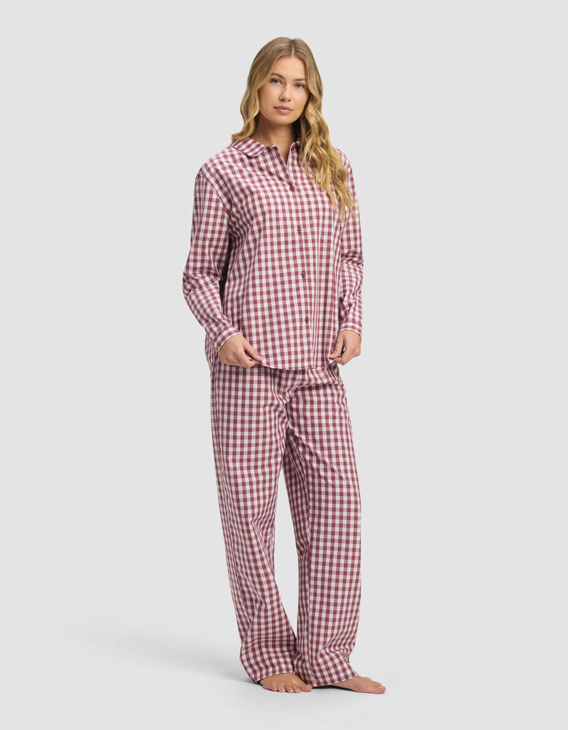 A woman with long, wavy blonde hair poses barefoot against a plain light background wearing the Cozy Earth Women's Sutton Long Sleeve Pajama Set featuring a red and white checkered shirt and matching pants.