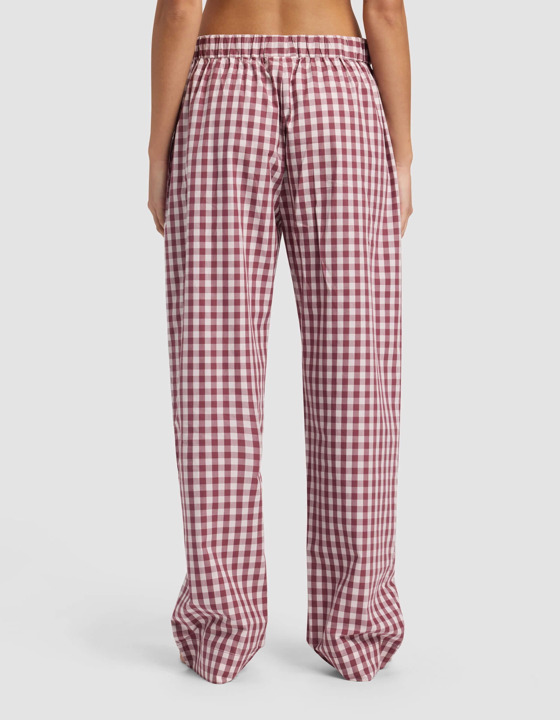 A person stands with their back to the camera, wearing Cozy Earth's Women's Sutton Pajama Pant—loose-fitting, high-waisted, red and white checkered with an elastic waistband—against a plain white background.|Color:Mulberry Gingham