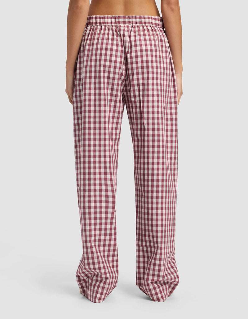 A person stands with their back to the camera, wearing Cozy Earth's Women's Sutton Pajama Pant—loose-fitting, high-waisted, red and white checkered with an elastic waistband—against a plain white background.