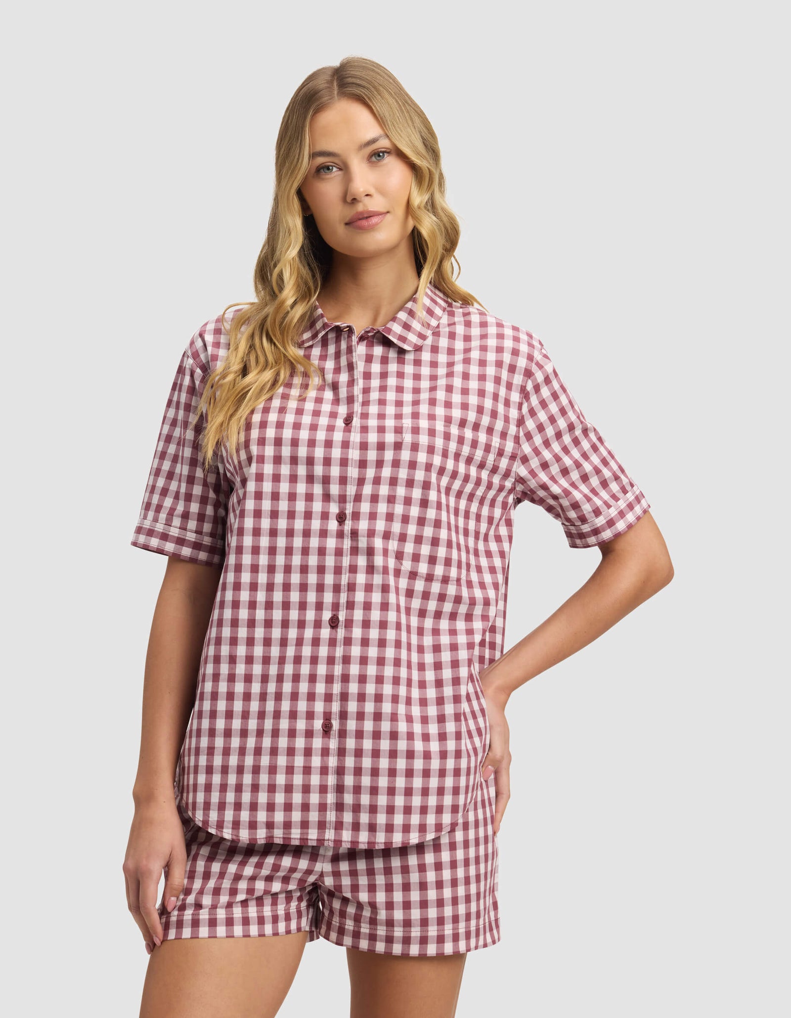 A woman with long, wavy blonde hair models the Cozy Earth Women's Sutton Short Sleeve Pajama Set in red and white gingham, standing against a plain light gray background.