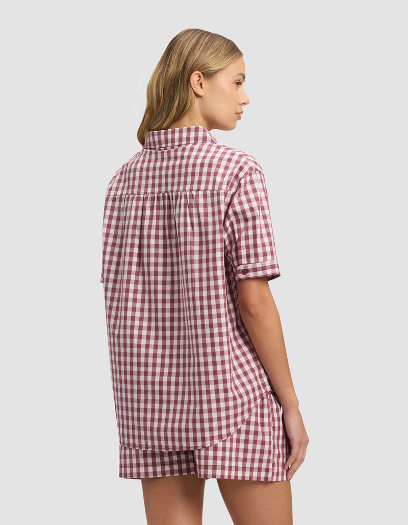 A woman with light brown hair, seen from behind against a plain light background, wears the Cozy Earth Women's Sutton Short Sleeve Pajama Top in an oversized red and white gingham pattern with matching shorts.