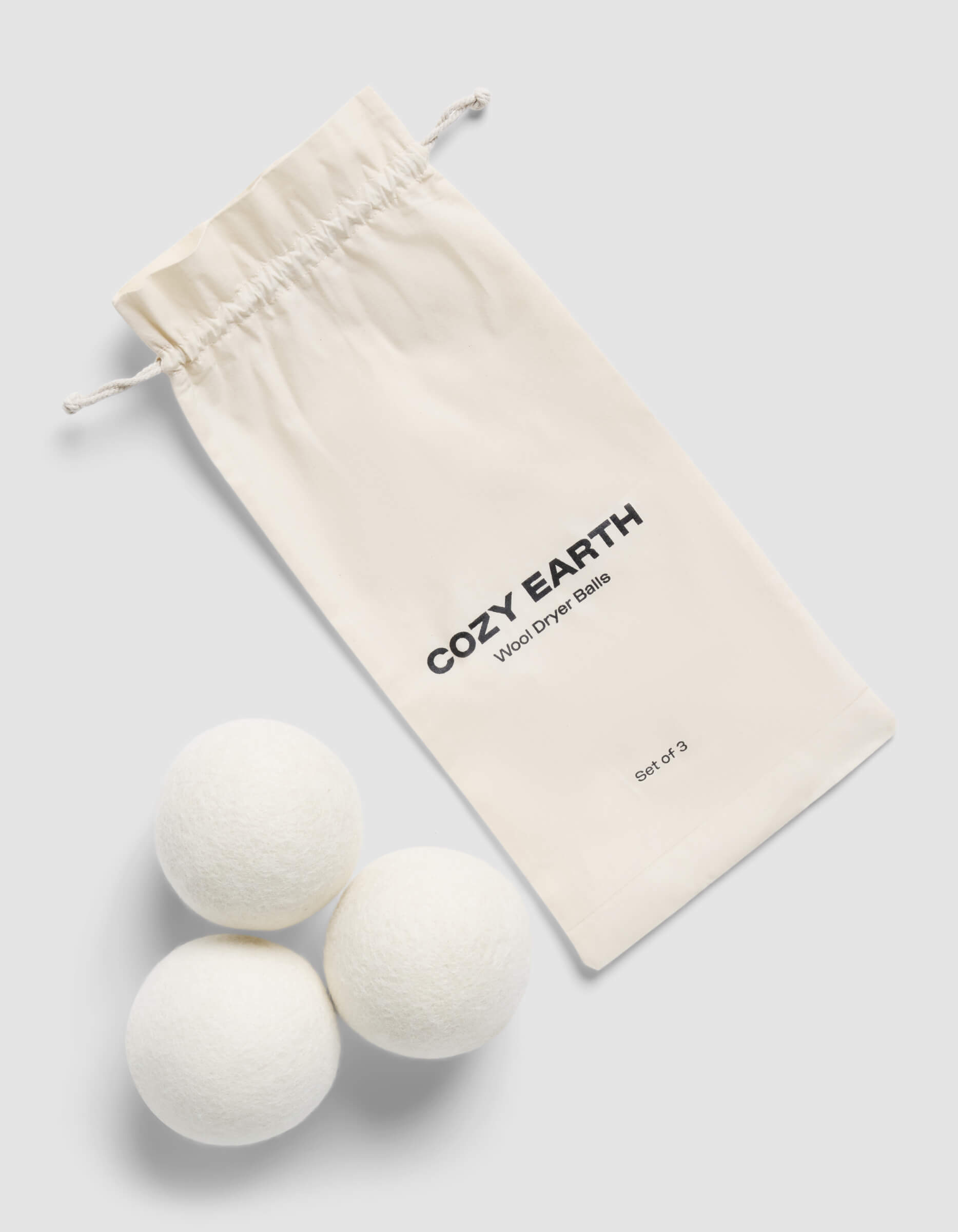 Three white Cozy Earth Dryer Balls with a Cozy Earth drawstring bag on a light gray background 