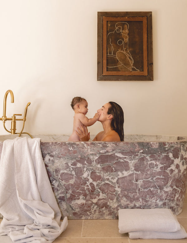 a woman sits in a marble bathtub holding a baby
