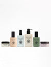 The Day-to-Night Essentials collection from Cozy Earth is neatly arranged in a row, featuring bottles and jars of different sizes and colors. Each item has a minimalistic label that showcases the Cozy Earth logo and product names.