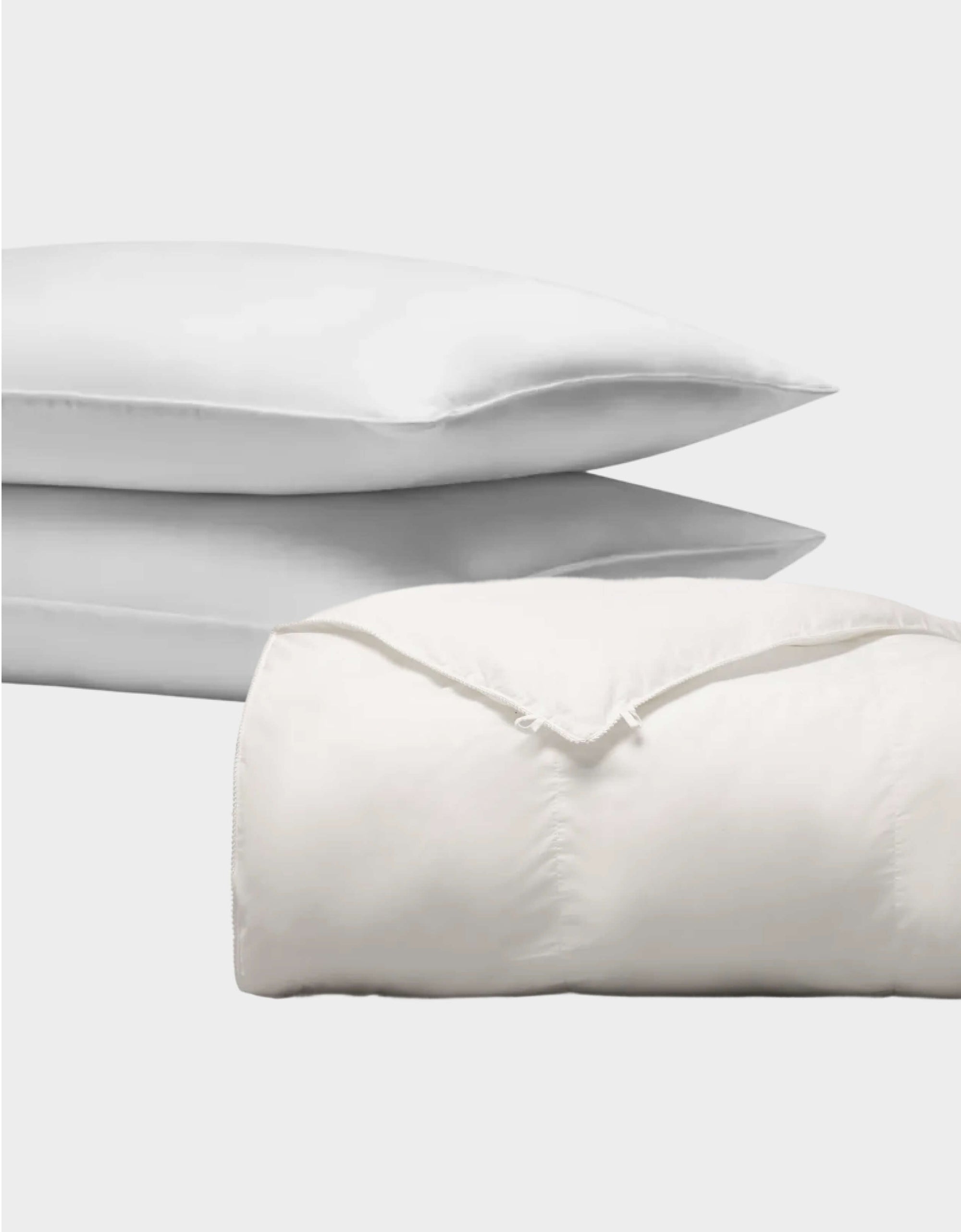 The Cozy Earth Down Alternative Insert Bundle features two white pillows stacked behind a neatly folded white comforter with visible seams and corner ties, all set against a plain, light background.