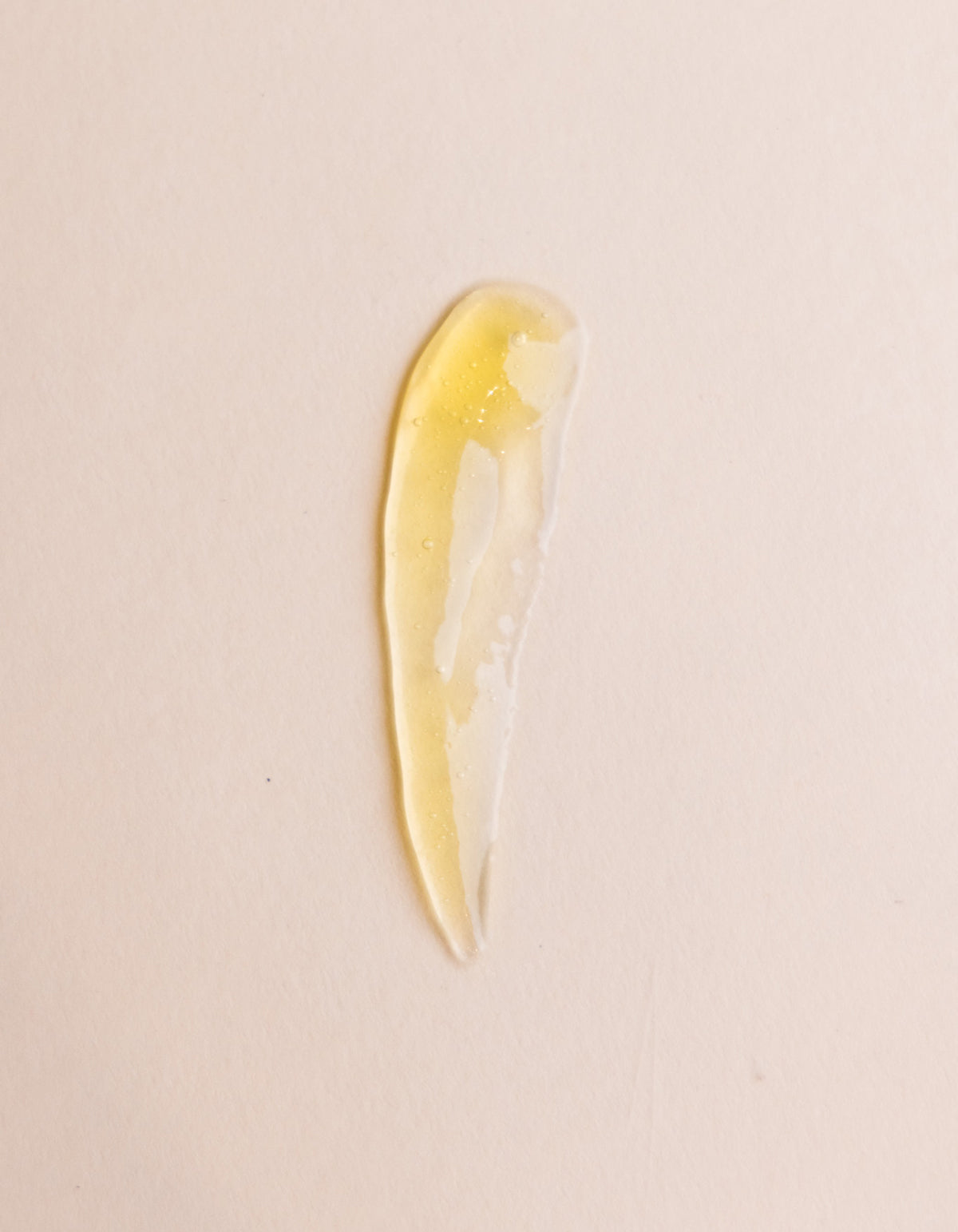 A translucent, yellow-tinted gel smear of Cozy Earth’s Enzyme Mask is spread in a curved, elongated shape on a light beige surface.|Size:Full Size