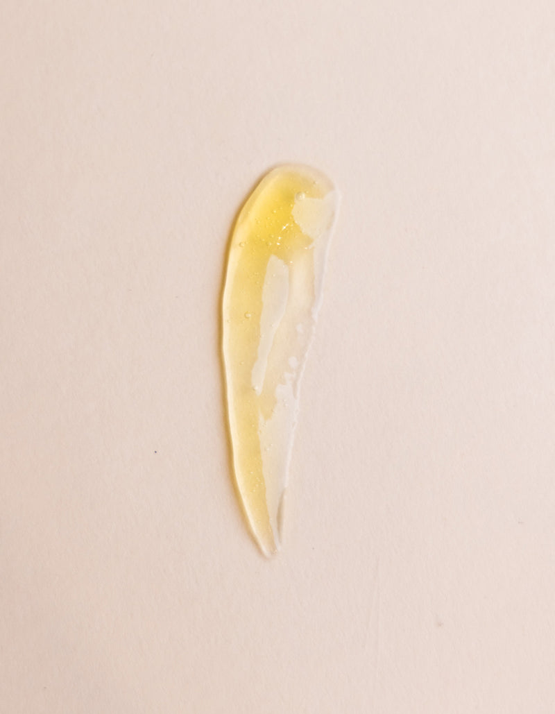 A translucent, yellow-tinted gel smear of Cozy Earth’s Enzyme Mask is spread in a curved, elongated shape on a light beige surface.