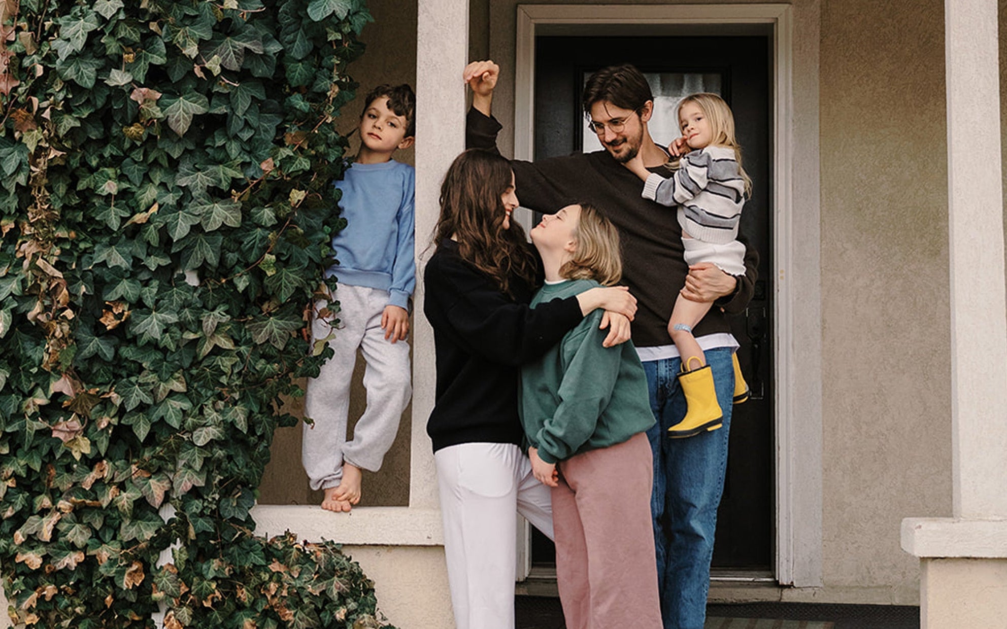 Family of four standing on the steps of a house with green ivy climbing the wall.