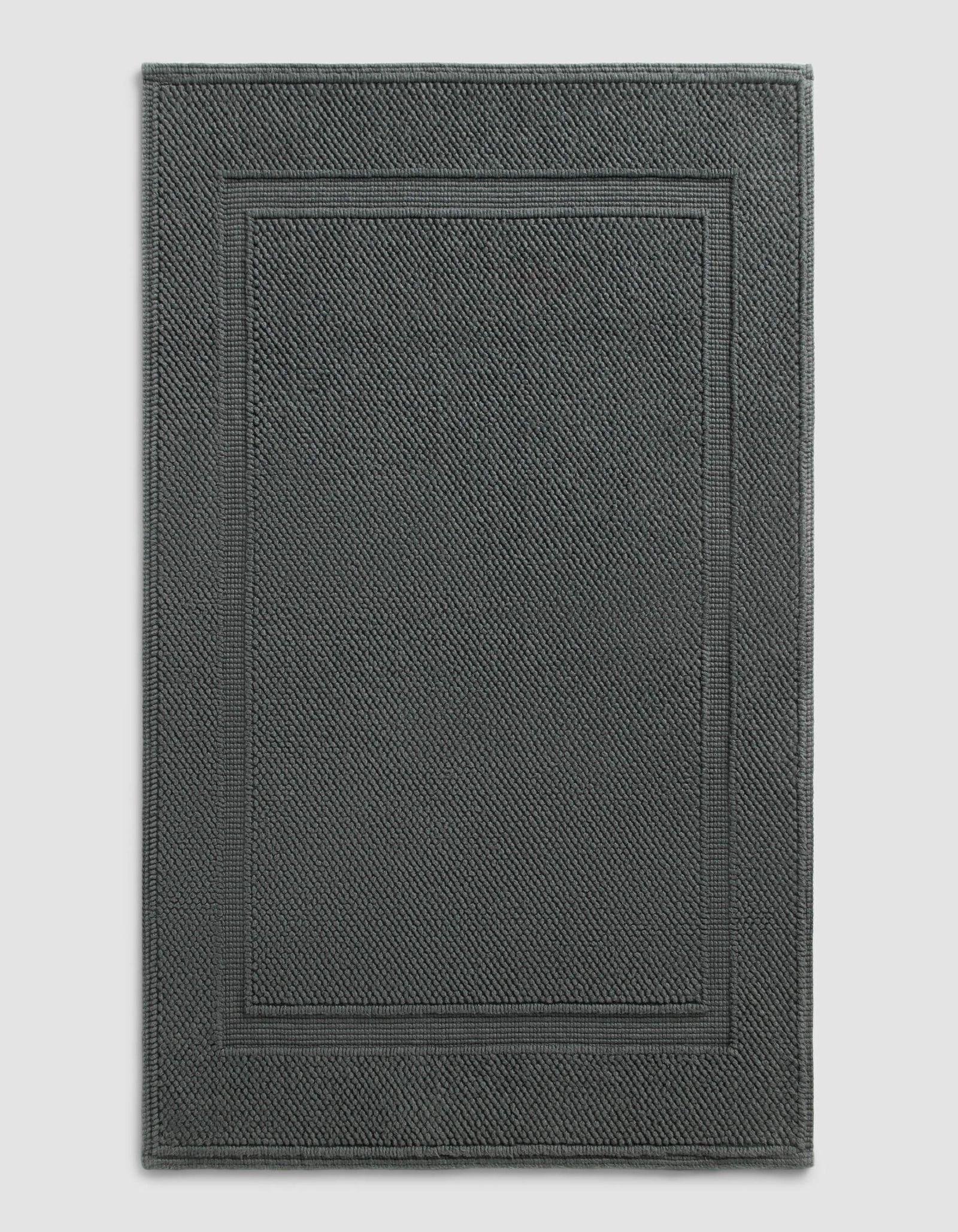 The Cozy Earth Classic Bath Mat features a dark gray, rectangular design with a textured surface and double border, shown against a plain light background.