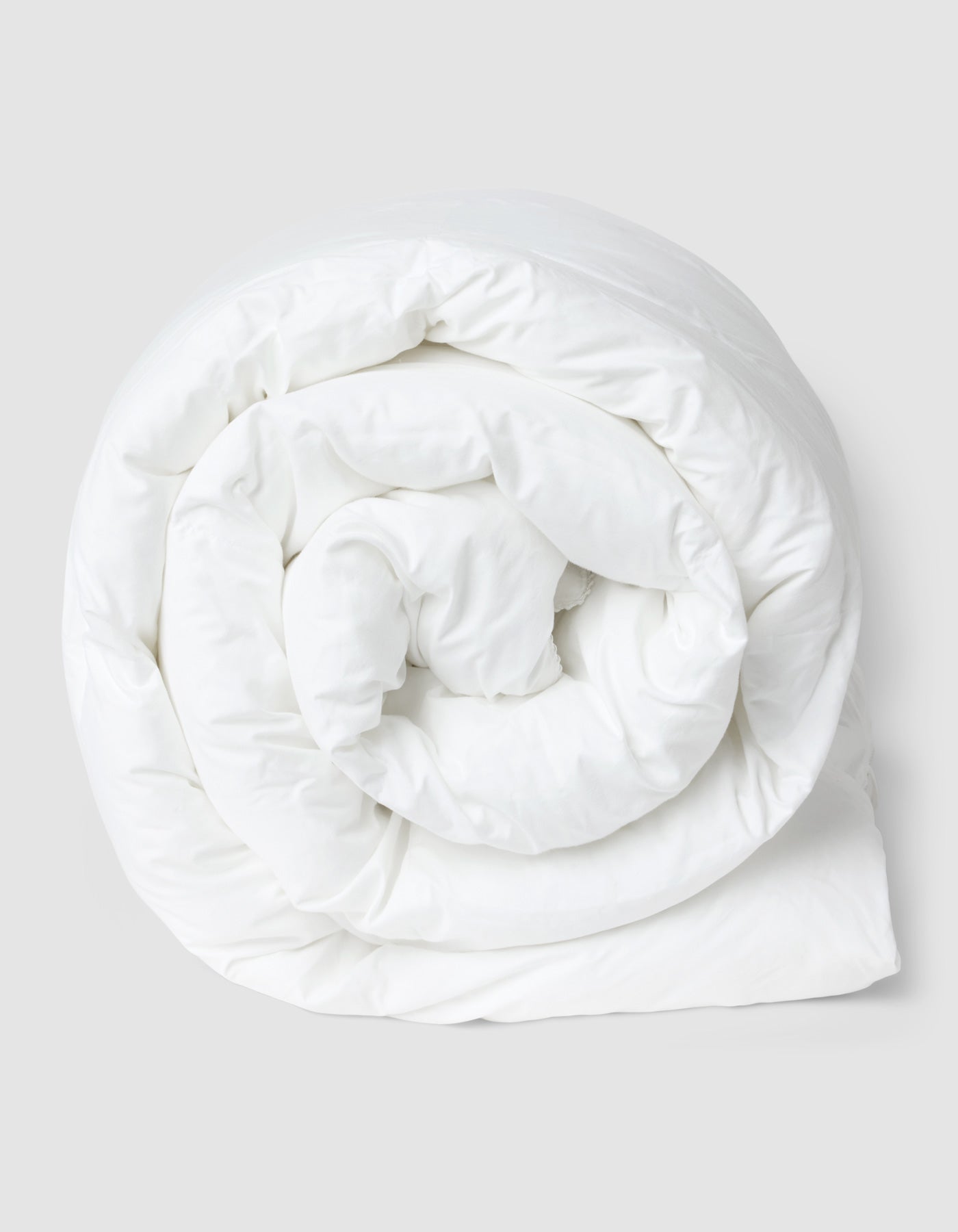 The Cozy Earth Down Alternative Comforter is rolled up in a spiral shape against a plain, light gray background.