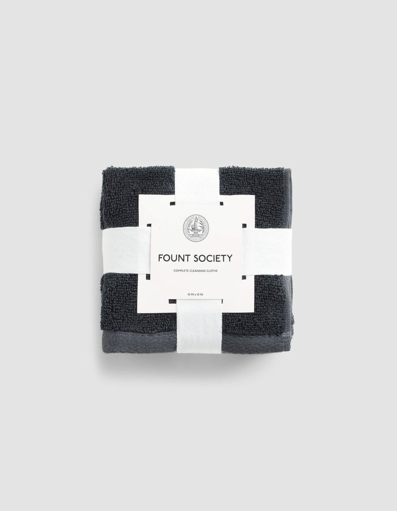 A set of dark gray Complete Cleansing Cloths by Cozy Earth, neatly folded and wrapped with a white paper band, displayed on a light gray background.