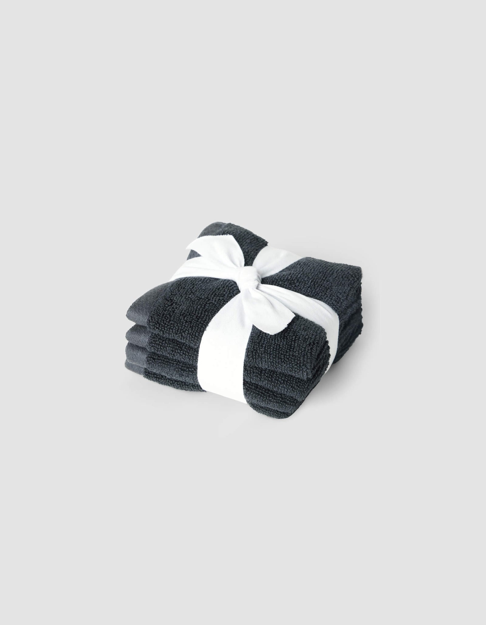 A neatly folded stack of Cozy Earth Complete Cleansing Cloths in dark gray, tied with a white ribbon, set against a plain light gray background.