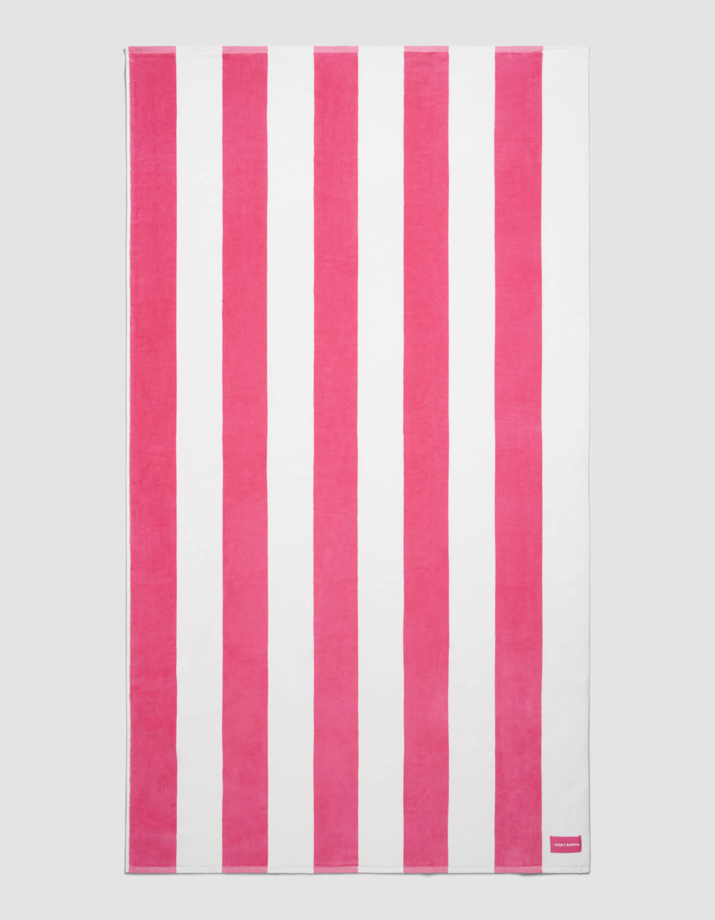 The Cozy Earth Seaside Resort Towel features alternating vertical pink and white stripes on a plain background, with a small pink tag displaying white text in one corner.