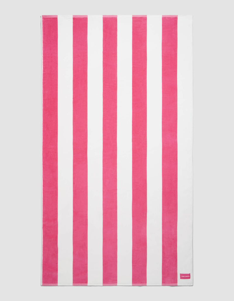 The Cozy Earth Seaside Resort Towel features alternating vertical pink and white stripes on a plain background, with a small pink tag displaying white text in one corner.