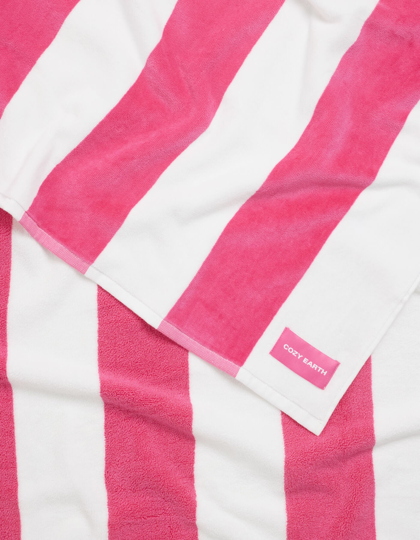 The Seaside Resort Towel by Cozy Earth, with bold pink and white vertical stripes, is laid out flat and features a small pink label in one corner reading "Cozy Earth.|Color:Punch Stripe