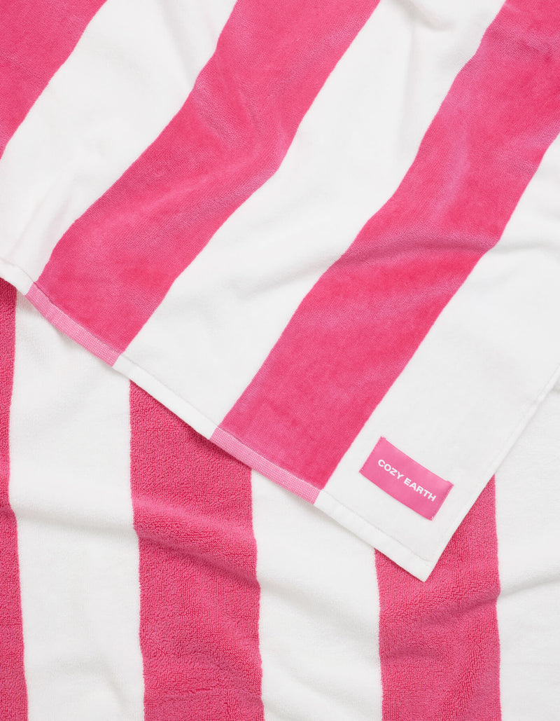 The Seaside Resort Towel by Cozy Earth, with bold pink and white vertical stripes, is laid out flat and features a small pink label in one corner reading "Cozy Earth.