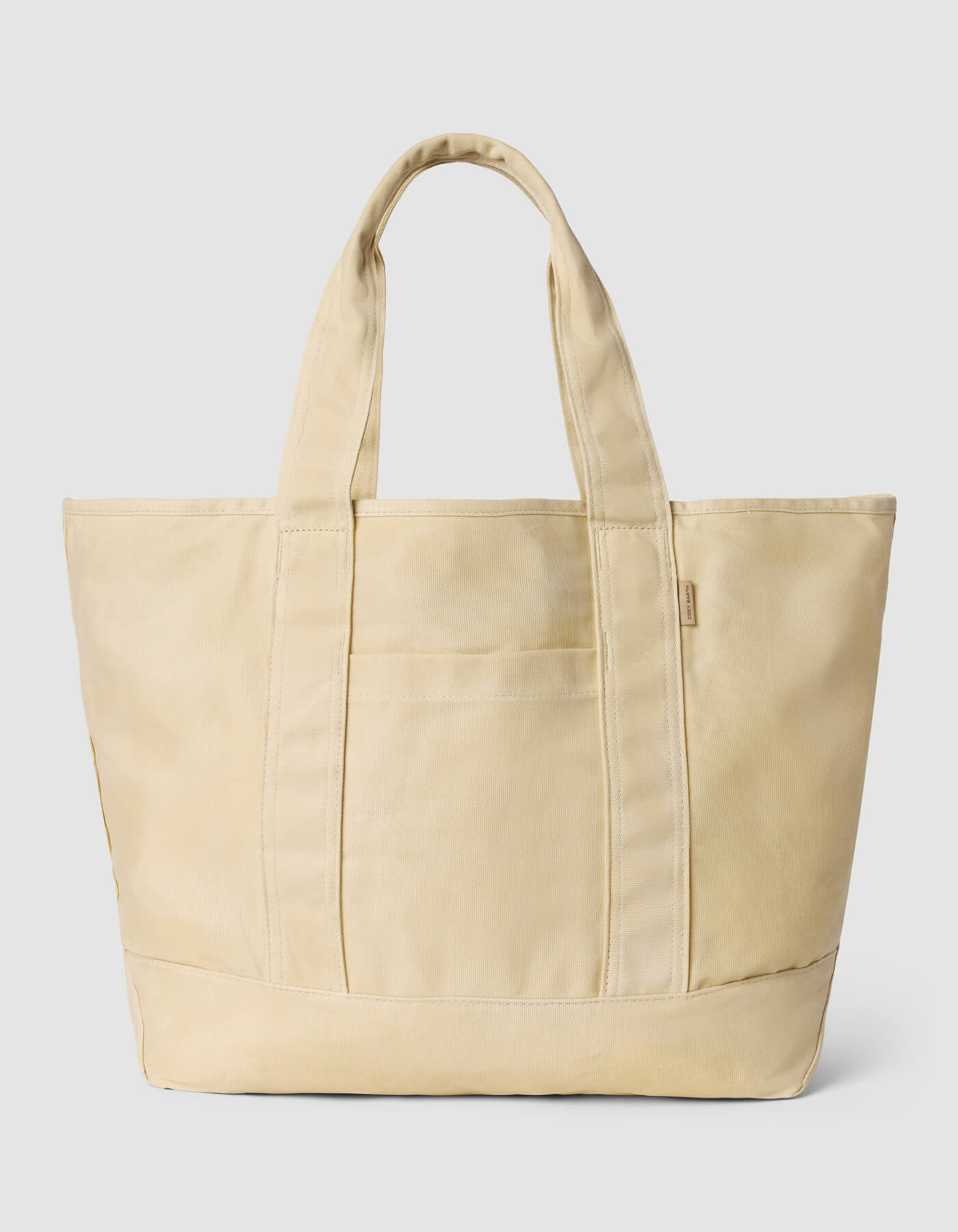 The Cozy Earth Waxed Canvas Tote, a spacious beige bag with two sturdy handles and a front pocket, is displayed against a plain light gray background.