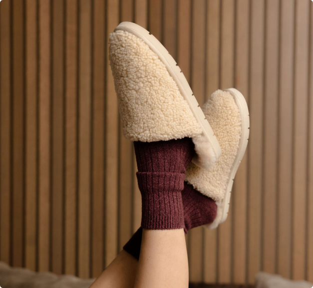 A person wearing Cozy Earth Puffy Sheep Slippers and Lounge Socks raise their feet in the air.