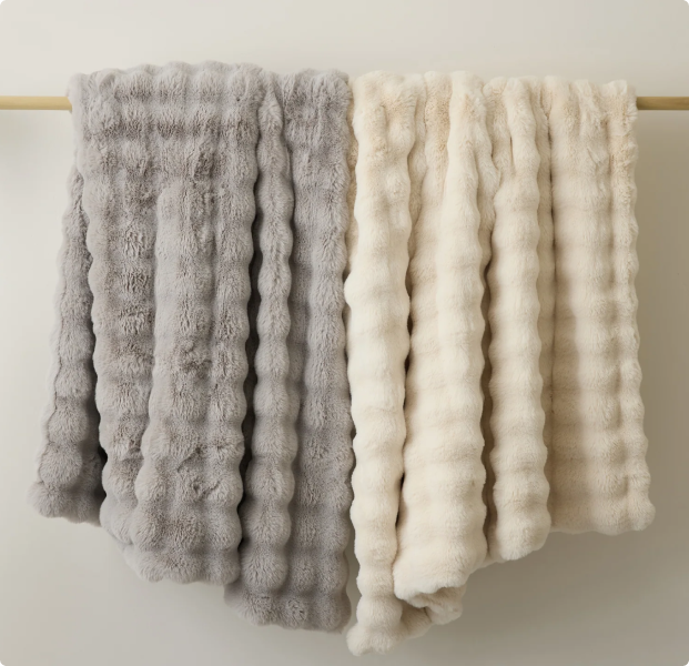 Two Cozy Earth Bubble Cuddle Blankets in Light Grey and Creme are draped over a wooden rod.