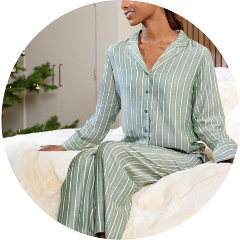 A woman wearing Cozy Earth Soft Woven Long Sleeve Pajamas sits on a bed.