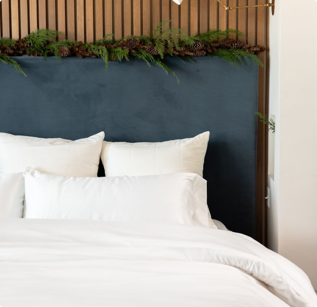 A bed with an evergreen garland along the headboard features Cozy Earth bedding.
