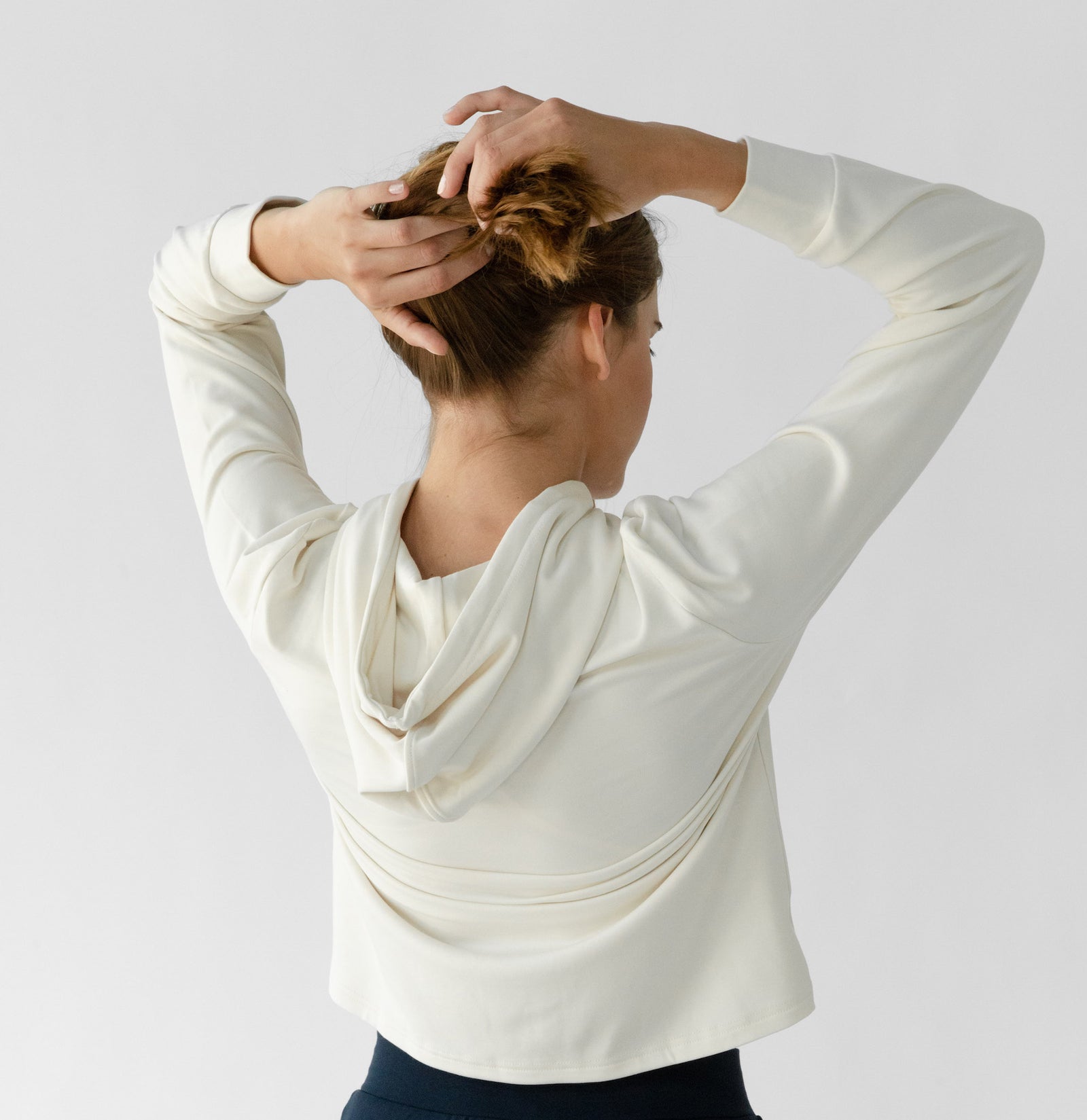 A person with brown hair, seen from behind against a white background, wears the Cozy Earth Women's Ultra-Soft Bamboo Wide Leg Pull On Pant & Hoodie Set while adjusting their hair. 