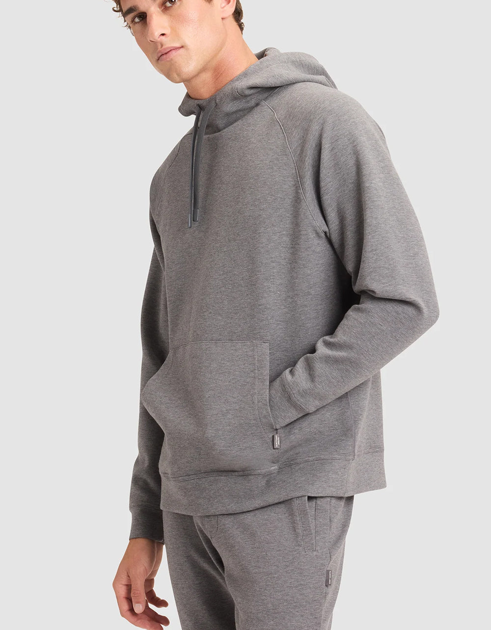 A man wearing a gray Cozy Earth StretchTech Hoodie and pants on a light gray background
